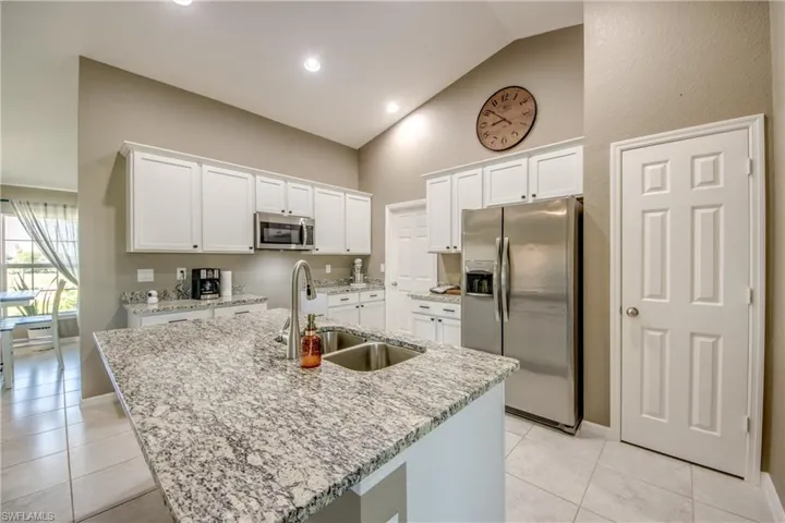 Kitchen with stainless steel appliances, white cabinetry, light tile patterned flooring, light stone countertops, and high vaulted ceiling