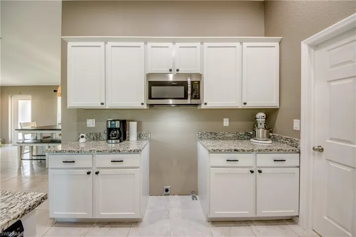 Kitchen with stainless steel microwave, white cabinetry, light stone countertops, and light tile patterned flooring