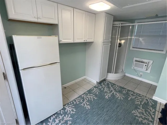 Kitchen with an AC wall unit, white cabinetry, fridge, and light tile patterned floors