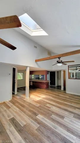 Living room with beamed ceiling, hardwood / wood-style flooring, high vaulted ceiling, ceiling fan, and a skylight