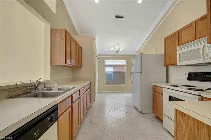 Kitchen featuring white appliances, ornamental molding, sink, and a notable chandelier