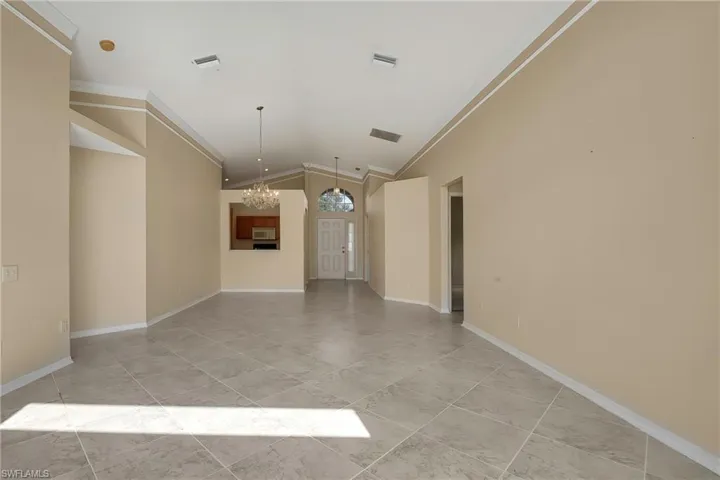 Unfurnished living room with ornamental molding, lofted ceiling, and an inviting chandelier