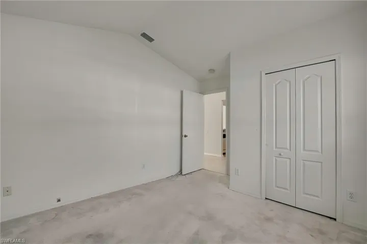 Unfurnished bedroom with light colored carpet, lofted ceiling, and a closet