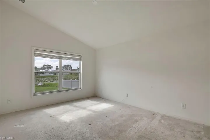 Carpeted empty room featuring vaulted ceiling