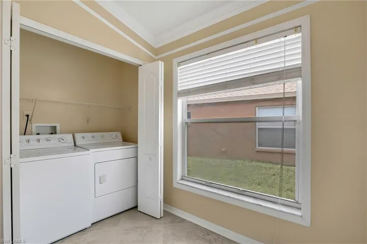 Washroom with ornamental molding, light tile patterned flooring, washer and dryer, and a healthy amount of sunlight