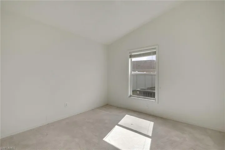 Carpeted empty room featuring vaulted ceiling