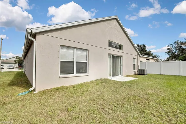 Rear view of house featuring central AC unit and a yard