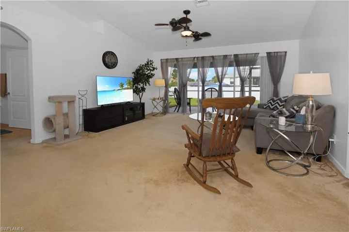 Living room featuring arched walkways, lofted ceiling, carpet, and ceiling fan