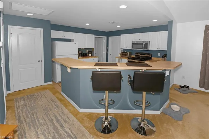 Kitchen with a breakfast bar area, appliances with stainless steel finishes, recessed lighting, white cabinetry, and light countertops