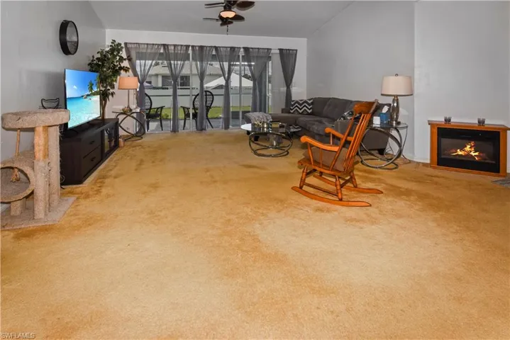 Living room with vaulted ceiling, light carpet, a glass covered fireplace, and ceiling fan