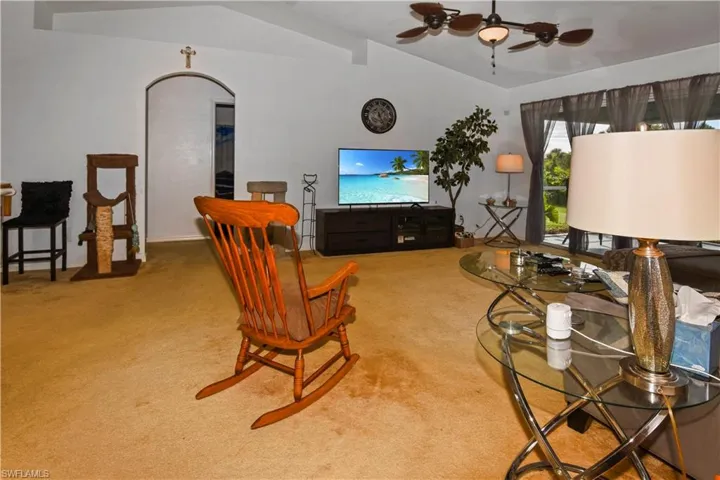 Living room featuring vaulted ceiling, ceiling fan, and carpet