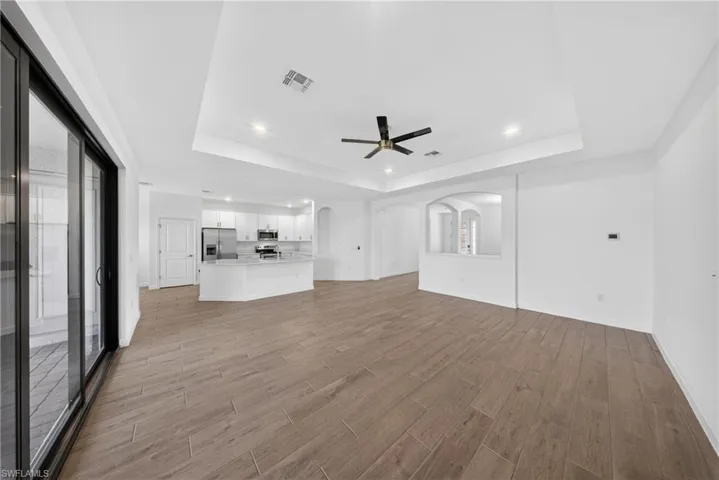 Expansive living area featuring wood-finish tile flooring and a tray ceiling with recessed lighting and a ceiling fan
