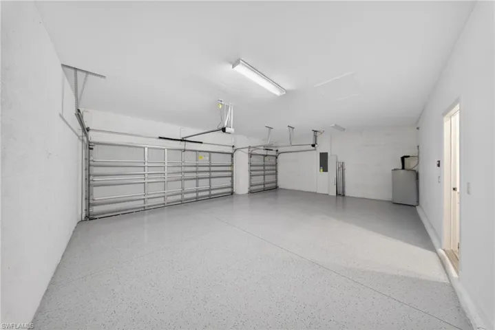 Spacious two-car garage featuring a light gray epoxy flooring, two overhead garage doors, bright overhead lighting, and an access door to the interior