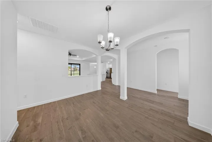 Expansive room featuring wood-finish flooring, a contemporary chandelier, and multiple arched doorways