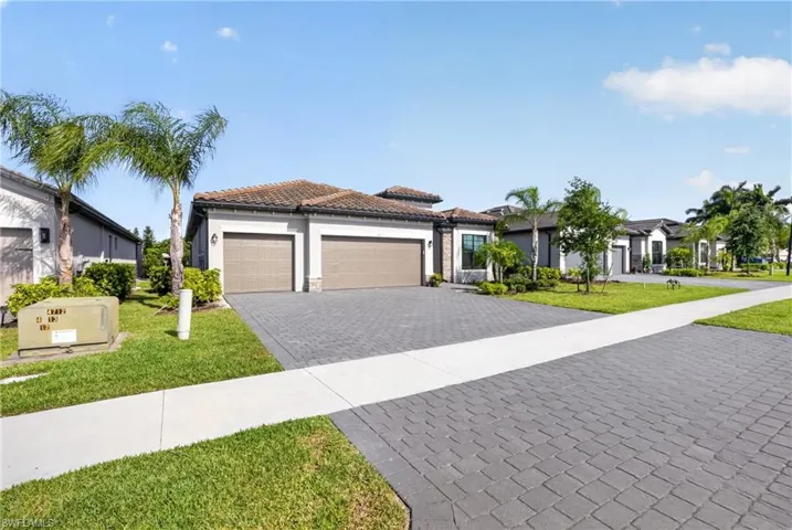Contemporary stucco exterior with a tile roof, dual garage doors, paver driveway, and mature palm trees