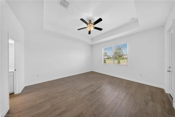Spacious room featuring wood-finish flooring, a tray ceiling with a ceiling fan, and a large window with horizontal blinds