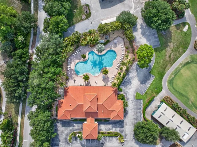 Spanish tile-roofed building featuring a large freeform swimming pool, surrounding lounge areas, mature palm trees, and adjacent paved parking