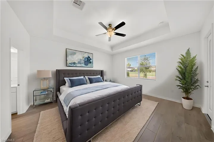 Tray ceiling with a ceiling fan, wood-finish flooring, white walls, and a large window with blinds