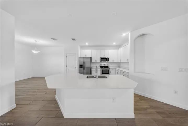 Open-concept kitchen featuring an expansive island with a stainless steel sink, white cabinetry, integrated stainless steel appliances, and recessed lighting