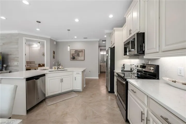 Kitchen featuring stainless steel appliances, white cabinetry, a kitchen island with sink, ornamental molding, and decorative light fixtures