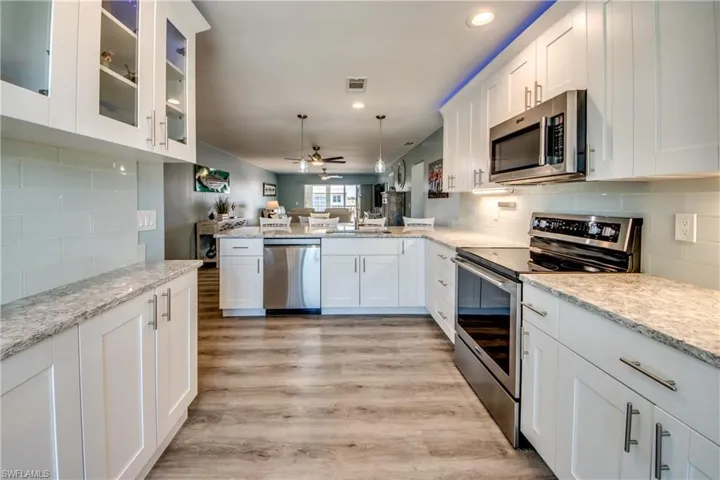 Kitchen with white cabinetry, light wood-type flooring, stainless steel appliances, tasteful backsplash, and ceiling fan