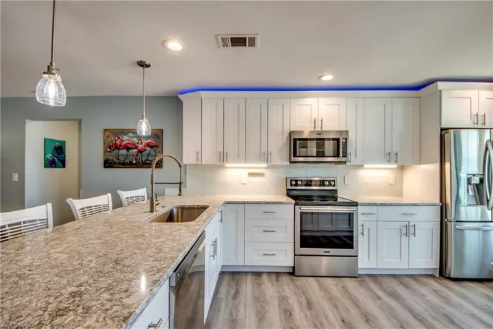 Kitchen with hanging light fixtures, light hardwood / wood-style flooring, stainless steel appliances, backsplash, and sink