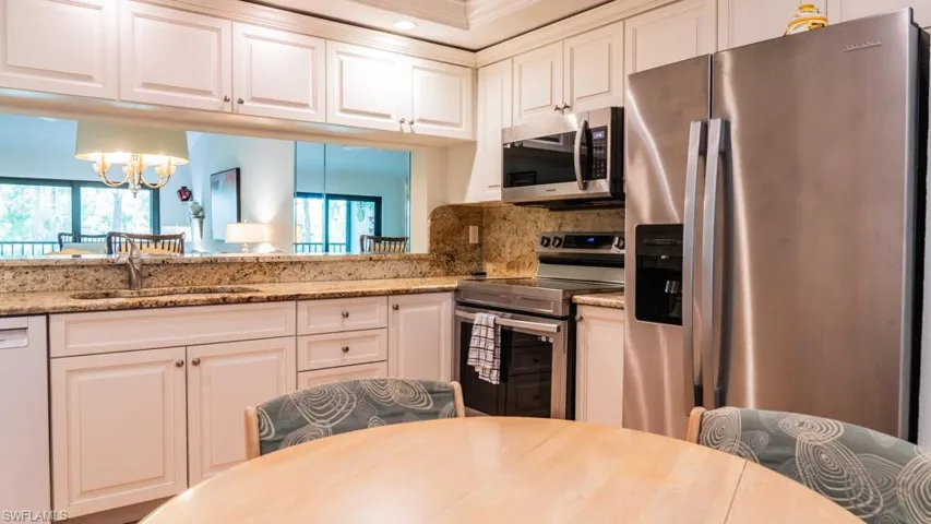 Kitchen with stainless steel appliances, healthy amount of natural light, a chandelier, white cabinetry, and crown molding
