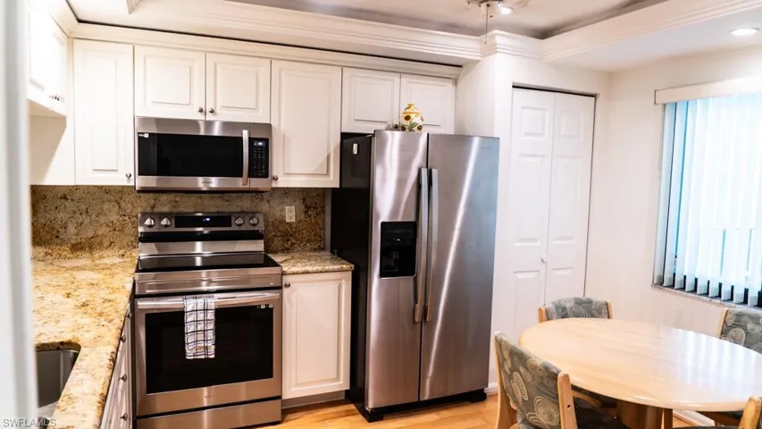 Kitchen featuring appliances with stainless steel finishes, ornamental molding, white cabinets, light wood-style flooring, and light stone countertops