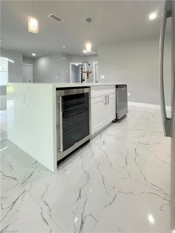 Kitchen with hanging light fixtures, wine cooler, and white cabinetry