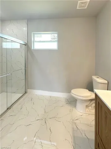 Bathroom featuring toilet, walk in shower, and vanity