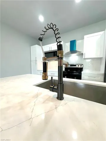 Room details featuring white cabinets, wall chimney range hood, concrete flooring, appliances with stainless steel finishes, and decorative backsplash