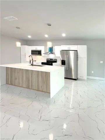 Kitchen featuring appliances with stainless steel finishes, a kitchen island with sink, sink, and white cabinets
