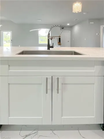 Kitchen with light stone counters, white cabinets, and sink