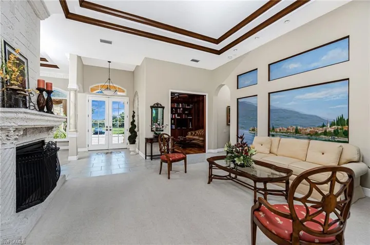 Living area featuring french doors, a high tray ceiling, light carpet, arched walkways, and a fireplace