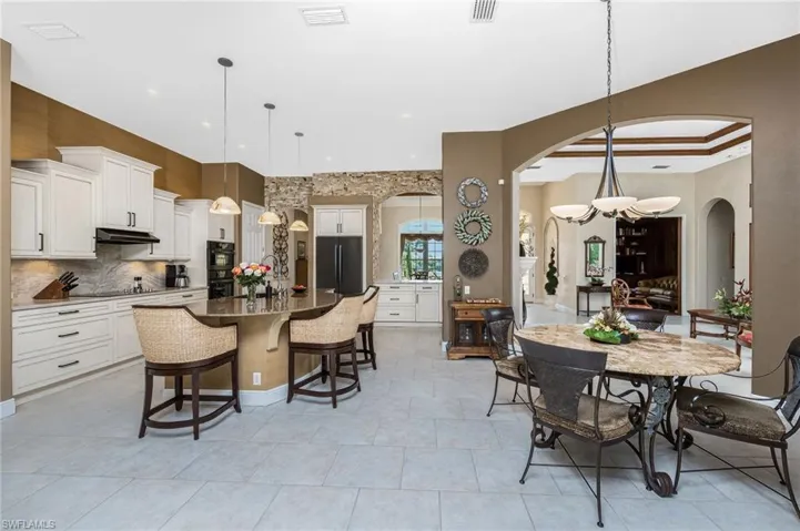Kitchen with a breakfast bar, white cabinets, an island with sink, and dark stone countertops