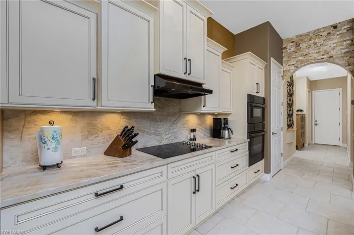 Kitchen featuring arched walkways, light stone countertops, black appliances, white cabinets, and decorative backsplash