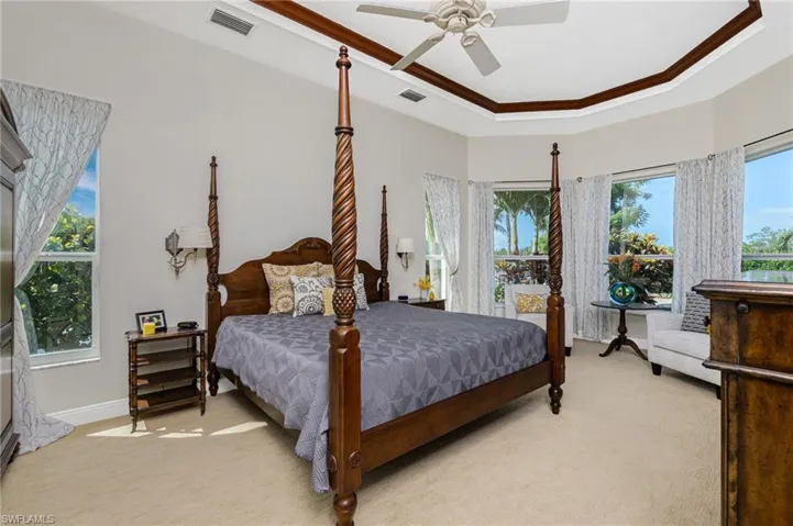 Bedroom with light carpet, multiple windows, ornamental molding, a ceiling fan, and a raised ceiling