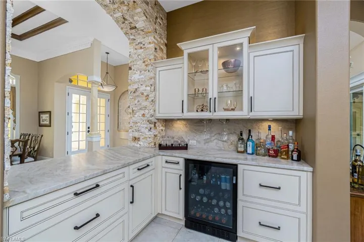 Indoor dry bar featuring arched walkways, beverage cooler, white cabinets, crown molding, and glass insert cabinets