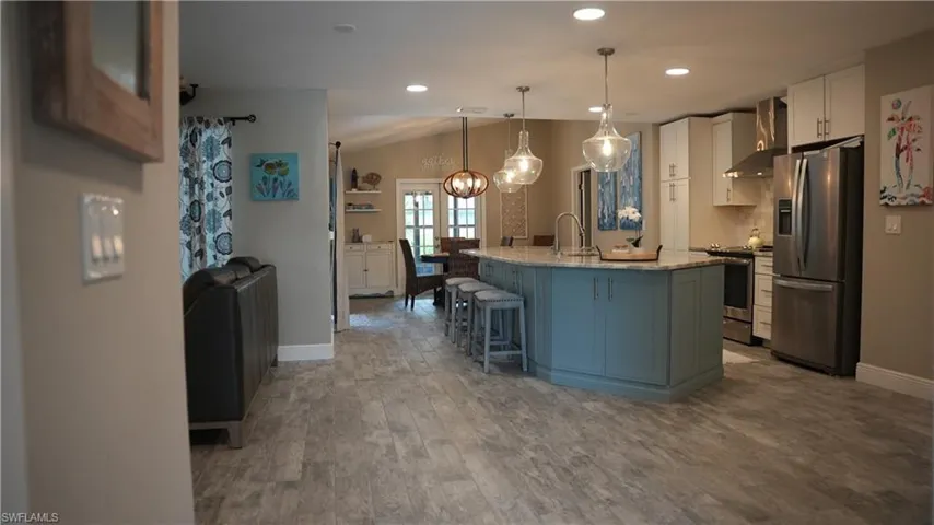 Kitchen featuring custom island, stainless steel appliances, a kitchen island with sink, dark wood-type flooring, and a breakfast bar area