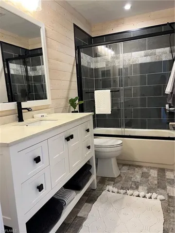 Full bath with vanity, stone finish flooring, combined bath / shower with glass door, and wooden walls