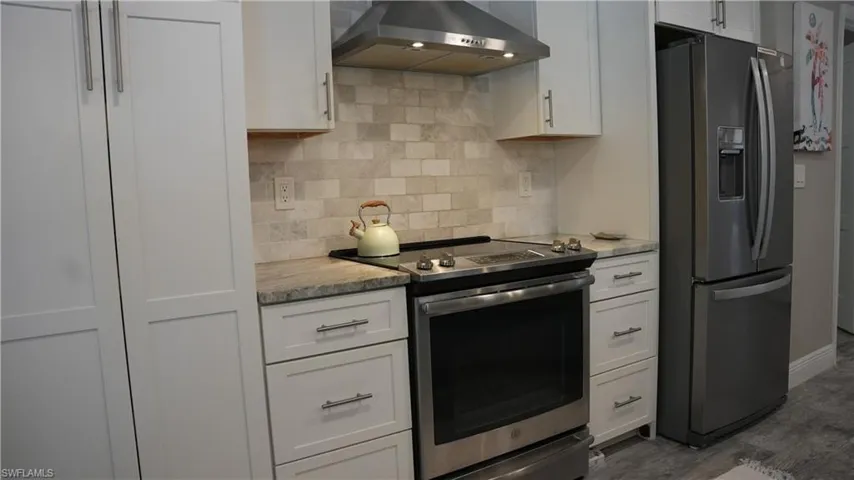 Kitchen with stainless steel appliances, white cabinets, light stone counters, dark wood finished floors, and decorative backsplash