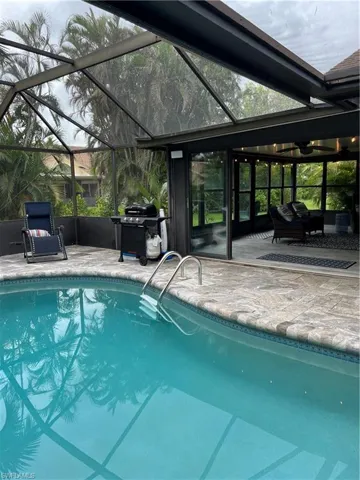 Outdoor pool with glass enclosure, a sunroom, area for grilling, and a patio area