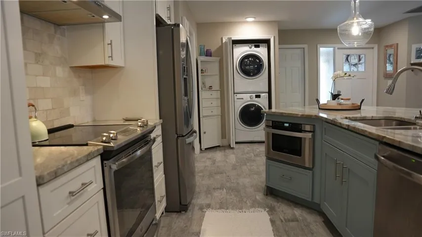 Dual tone kitchen featuring stainless steel appliances, light stone countertops, exhaust hood, two tone color scheme, and pendant lighting