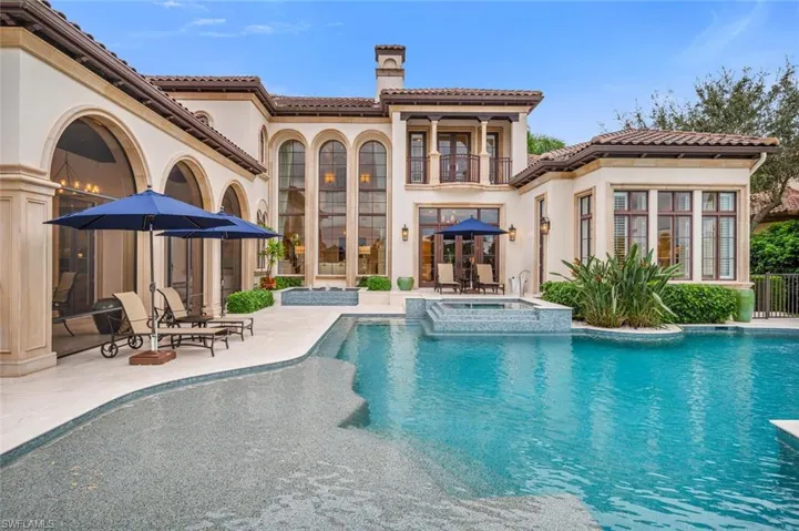 Rear view of house with stucco siding, a patio area, a pool with connected hot tub, a balcony, and a chimney