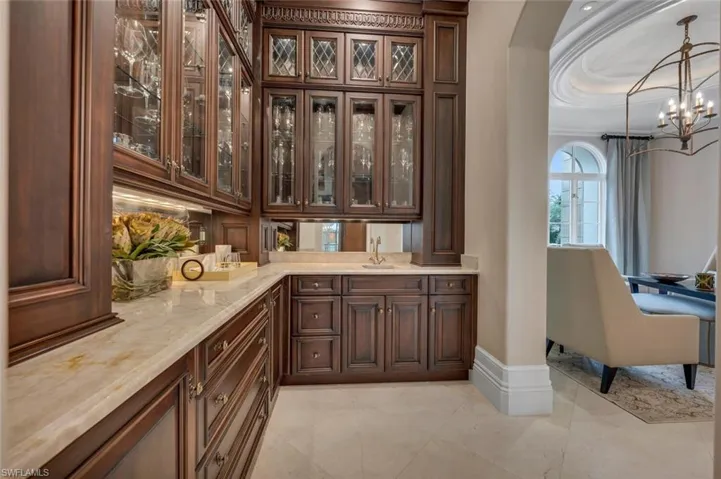 Bar featuring glass insert cabinets, dark brown cabinetry, decorative light fixtures, light stone countertops, and a chandelier
