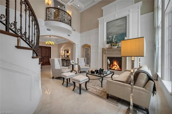 Living room with arched walkways, a chandelier, ornamental molding, a warm lit fireplace, and a high ceiling