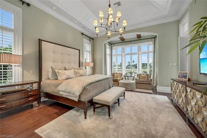 Bedroom with coffered ceiling, multiple windows, dark wood-style floors, and ornamental molding