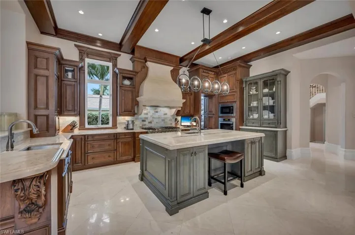 Kitchen featuring a kitchen bar, glass insert cabinets, light stone countertops, decorative light fixtures, and backsplash