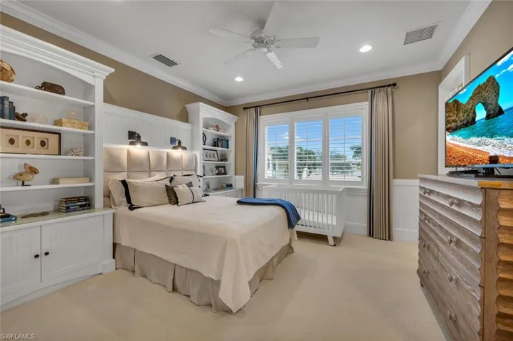 Bedroom featuring wainscoting, radiator heating unit, a decorative wall, ornamental molding, and ceiling fan
