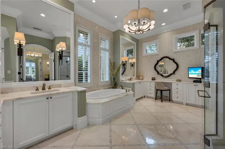 Full bathroom with a chandelier, inlaid floor details, two vanities, a bath, and crown molding